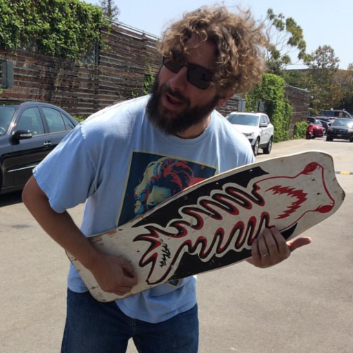 Bryan in sunglasses holding a hand-painted art board outdoors